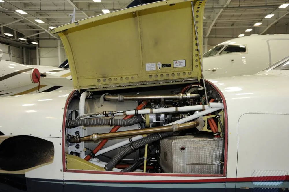 The engine compartment of a TBM 850 aircraft with the cowling open, revealing internal components and wiring.