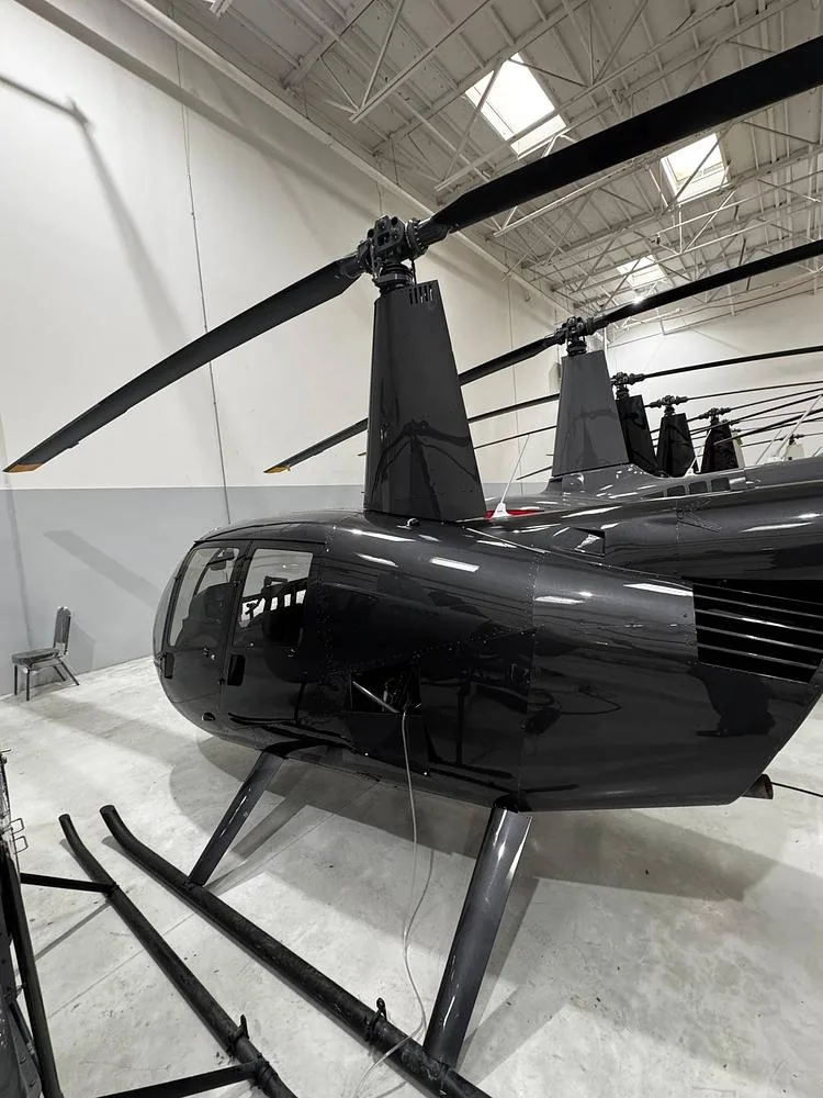 The rear-right side of a black Robinson R44 helicopter parked in a hangar.