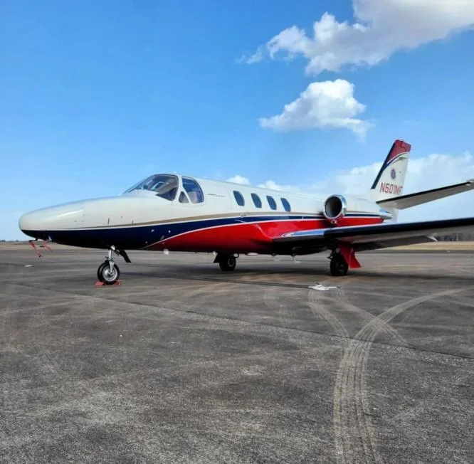 A white, blue, and red Cessna Citation business jet (N501MF) is parked on an asphalt tarmac under a blue sky.