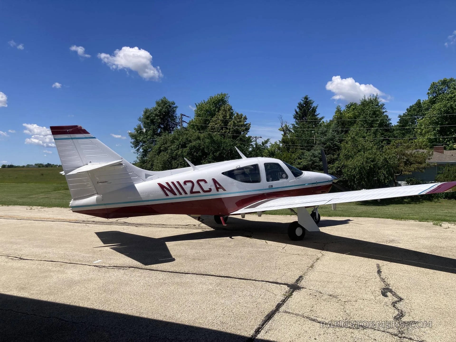 A white and red single-engine propeller aircraft (N112CA) parked on a concrete pad under a blue sky.