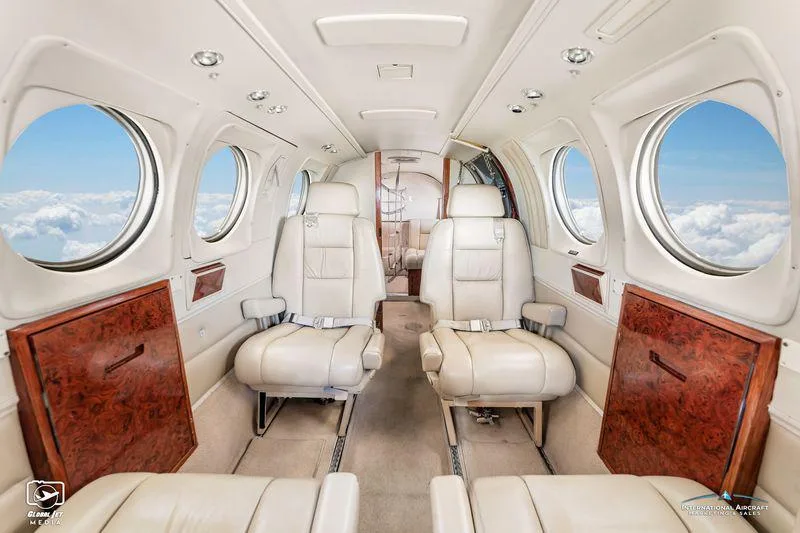 Interior view of an aircraft cabin with two rows of light-colored leather seats and wood paneling.