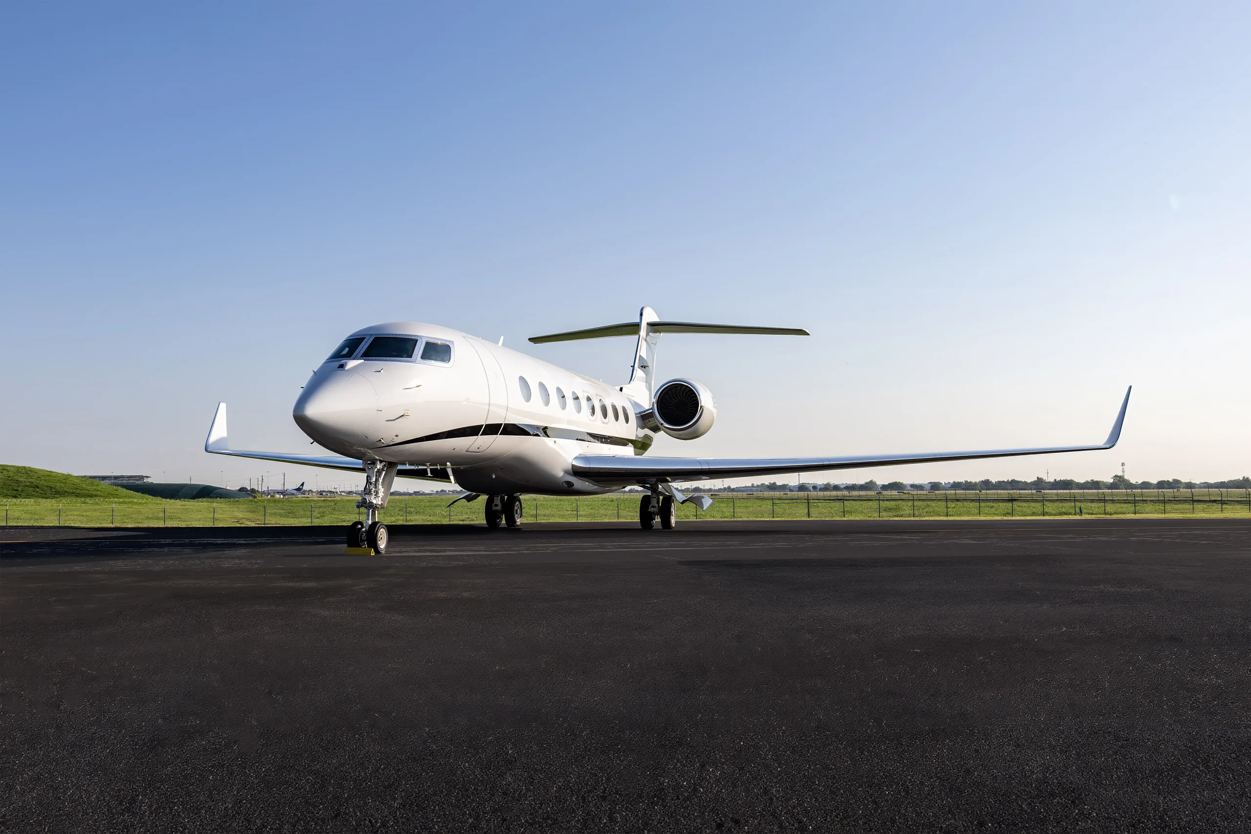 A sleek white Gulfstream G650 business jet is parked on an airport tarmac under a clear blue sky.