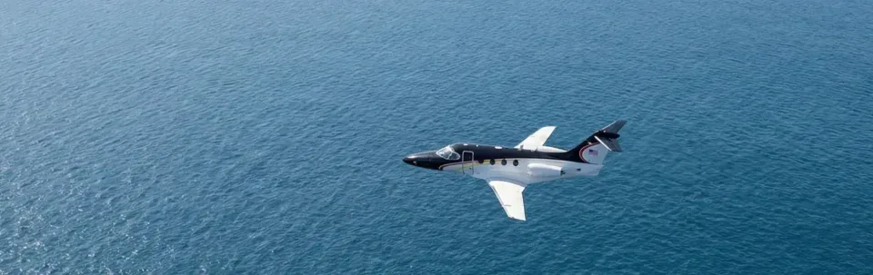 A black and white Hawker 400XP flying over the ocean.