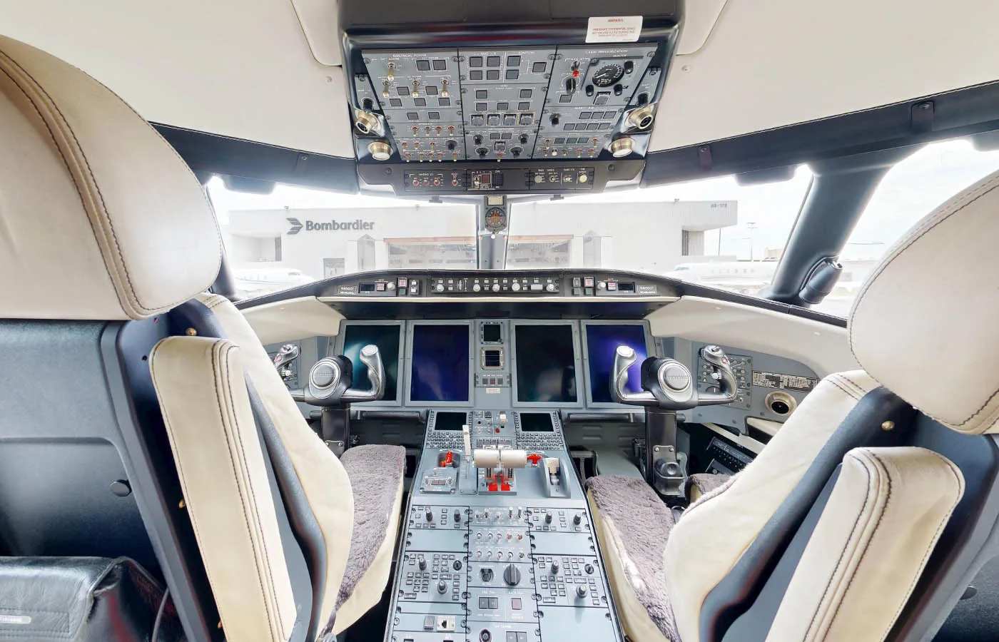 The cockpit of a Bombardier Challenger jet features multiple screens, control panels, and two pilot seats.