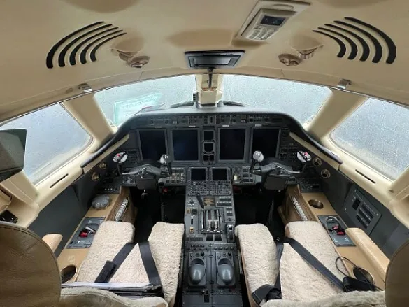 The cockpit of a business jet features a modern glass panel display and tan sheepskin seat covers.