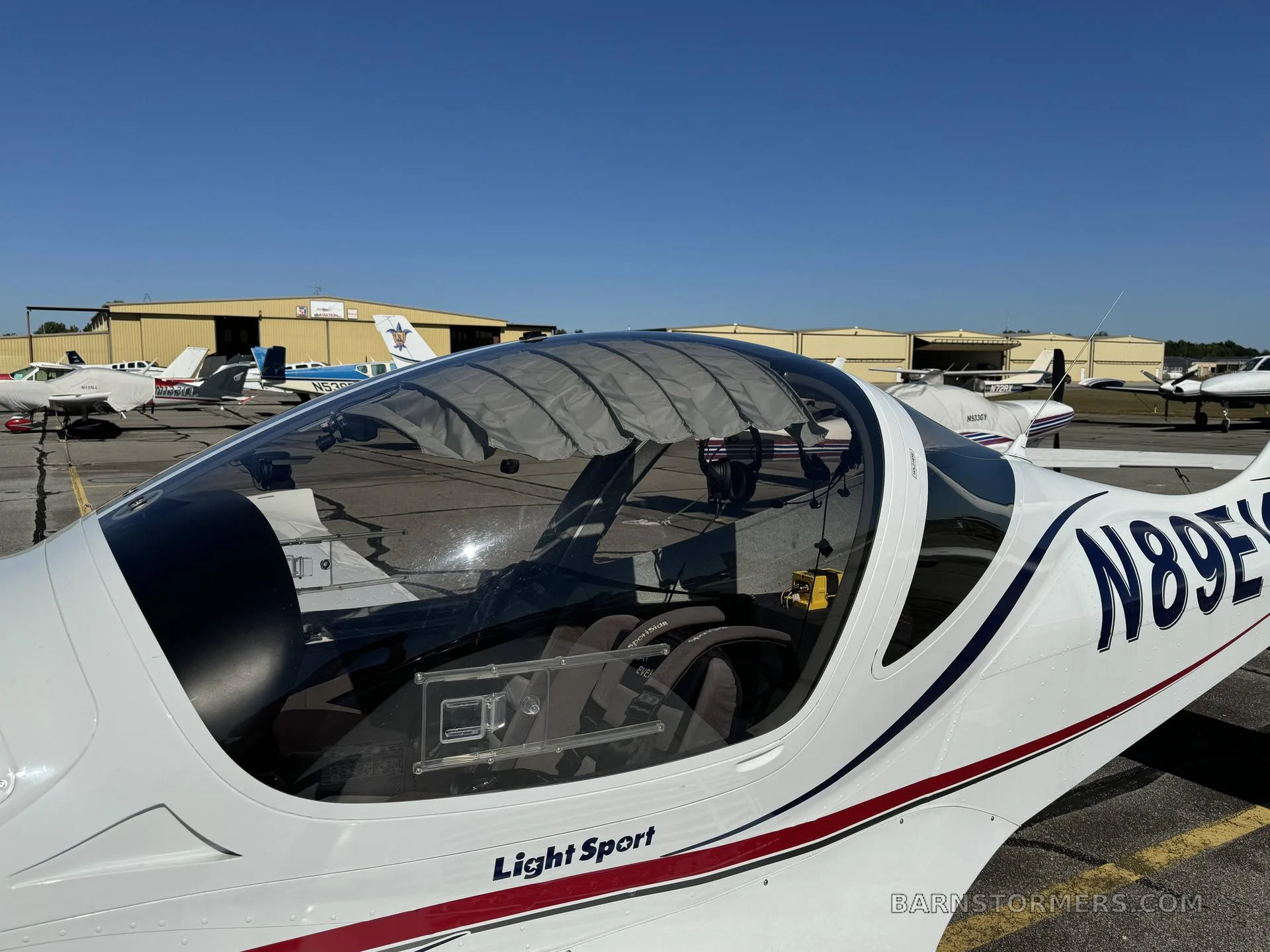 A close-up of the clear canopy and front fuselage of a white Evektor SportStar aircraft (N89EV) parked on an airfield.