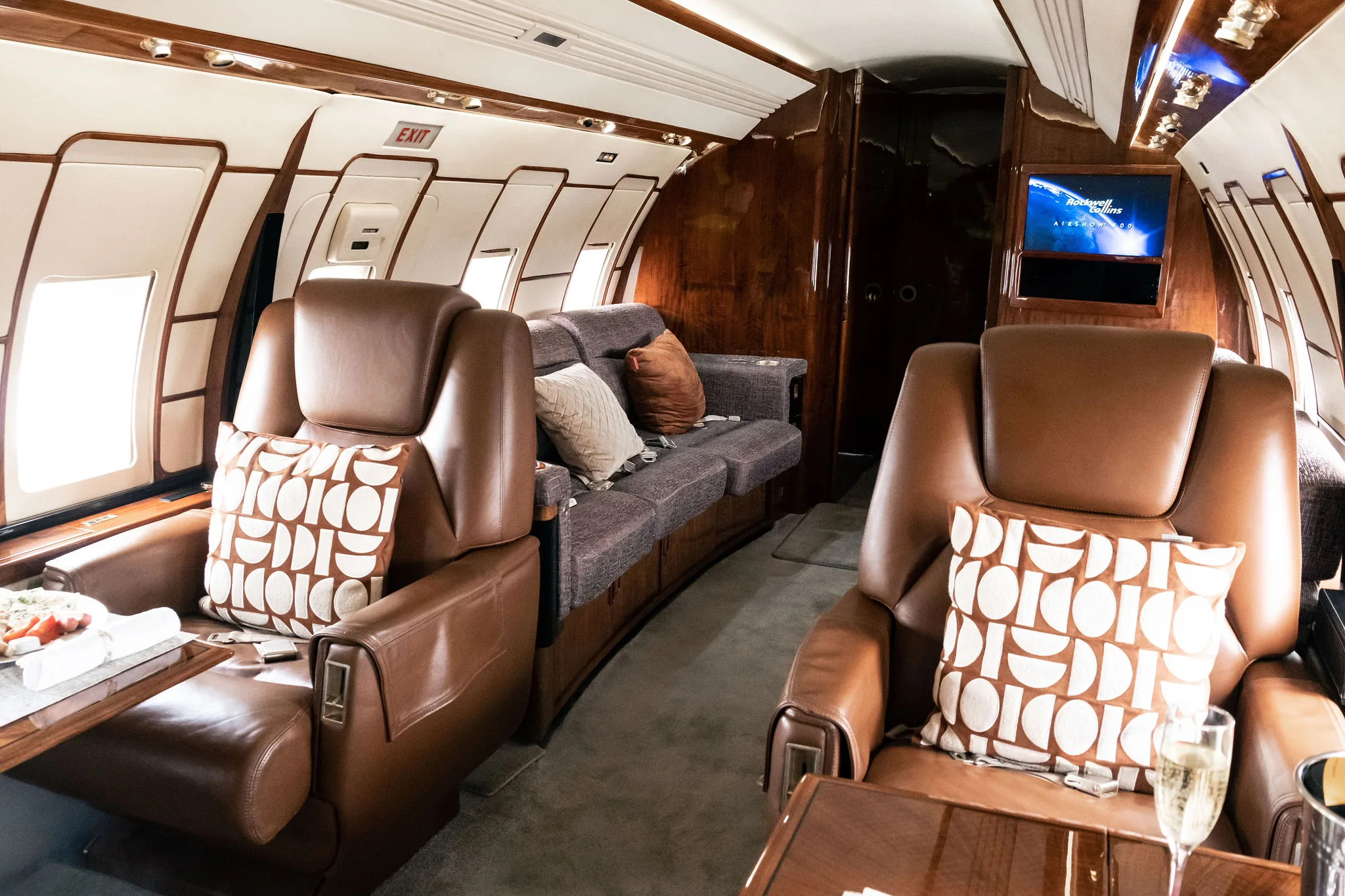Luxurious private jet interior with brown leather seats, a sofa, and a television screen.