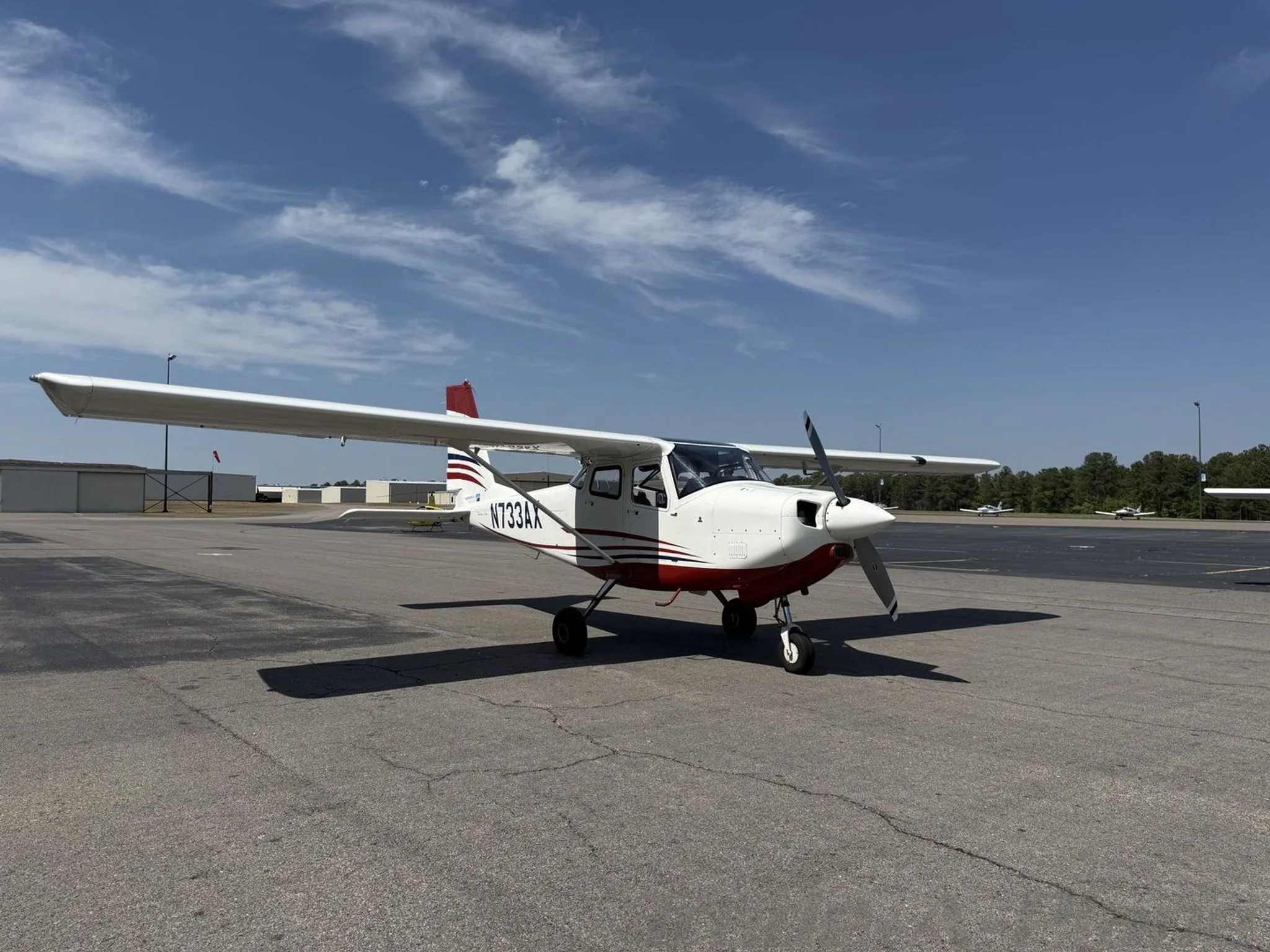White and red single-engine aircraft N733AX parked on an asphalt apron under a blue sky.