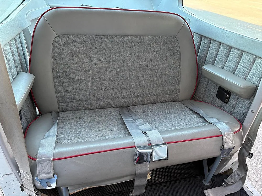 Close-up view of the gray fabric and leather rear seats with red piping and seatbelts in the aircraft cabin.
