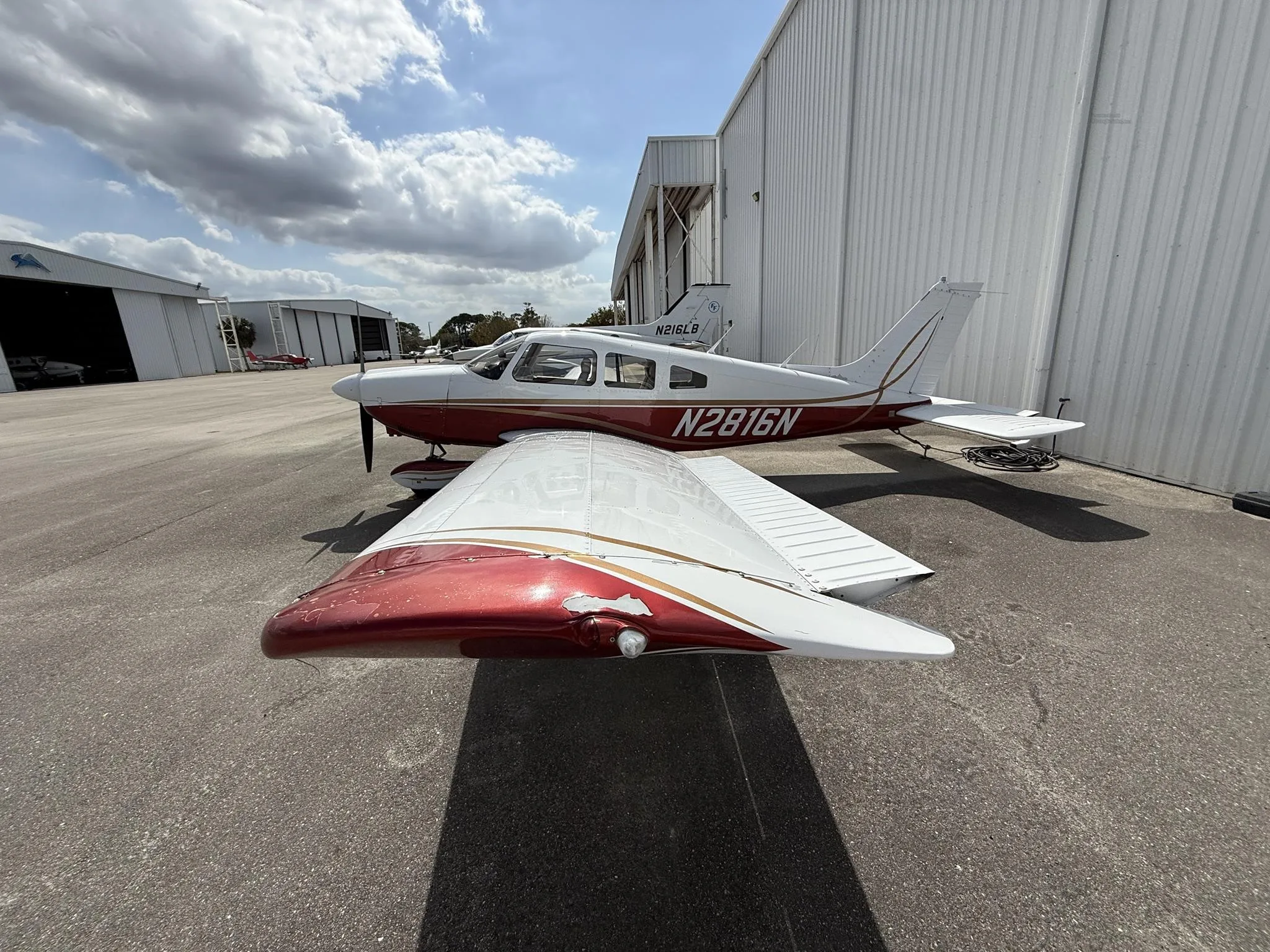 A side view of a white and red Piper PA-28-161 aircraft, N2816N, parked on an asphalt ramp with hangars in the background.