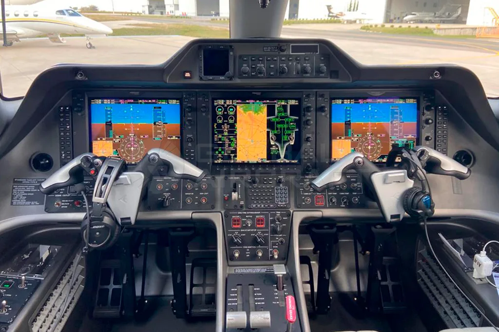 The cockpit of an Embraer Phenom 100, showing the instrument panel with multiple digital displays and controls.