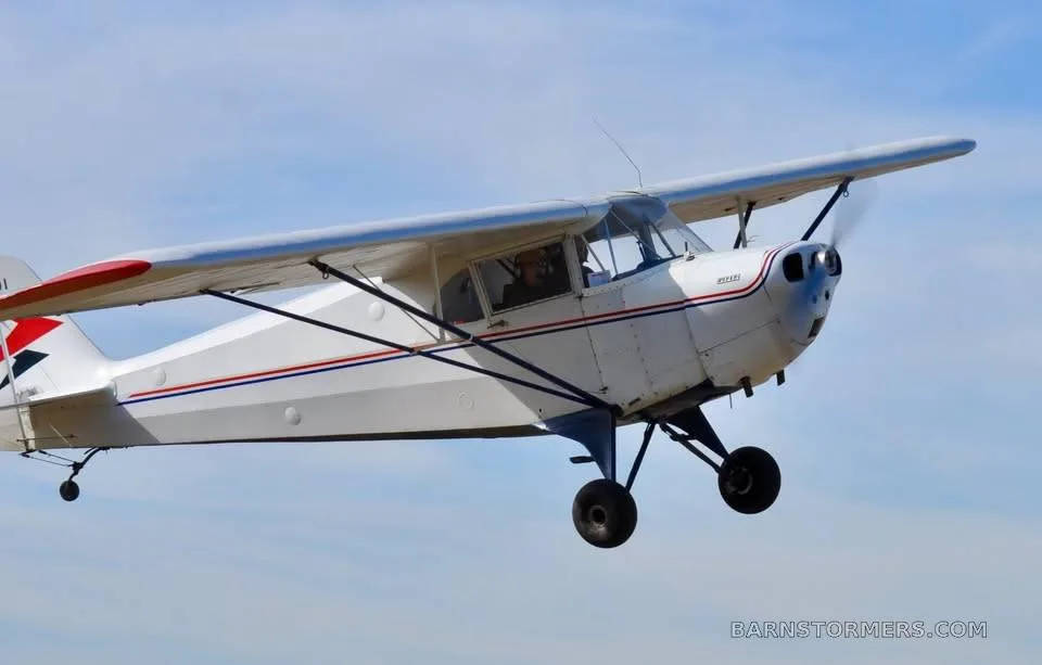 A white and red Piper Cub-style aircraft with registration N35001 flying against a blue sky.
