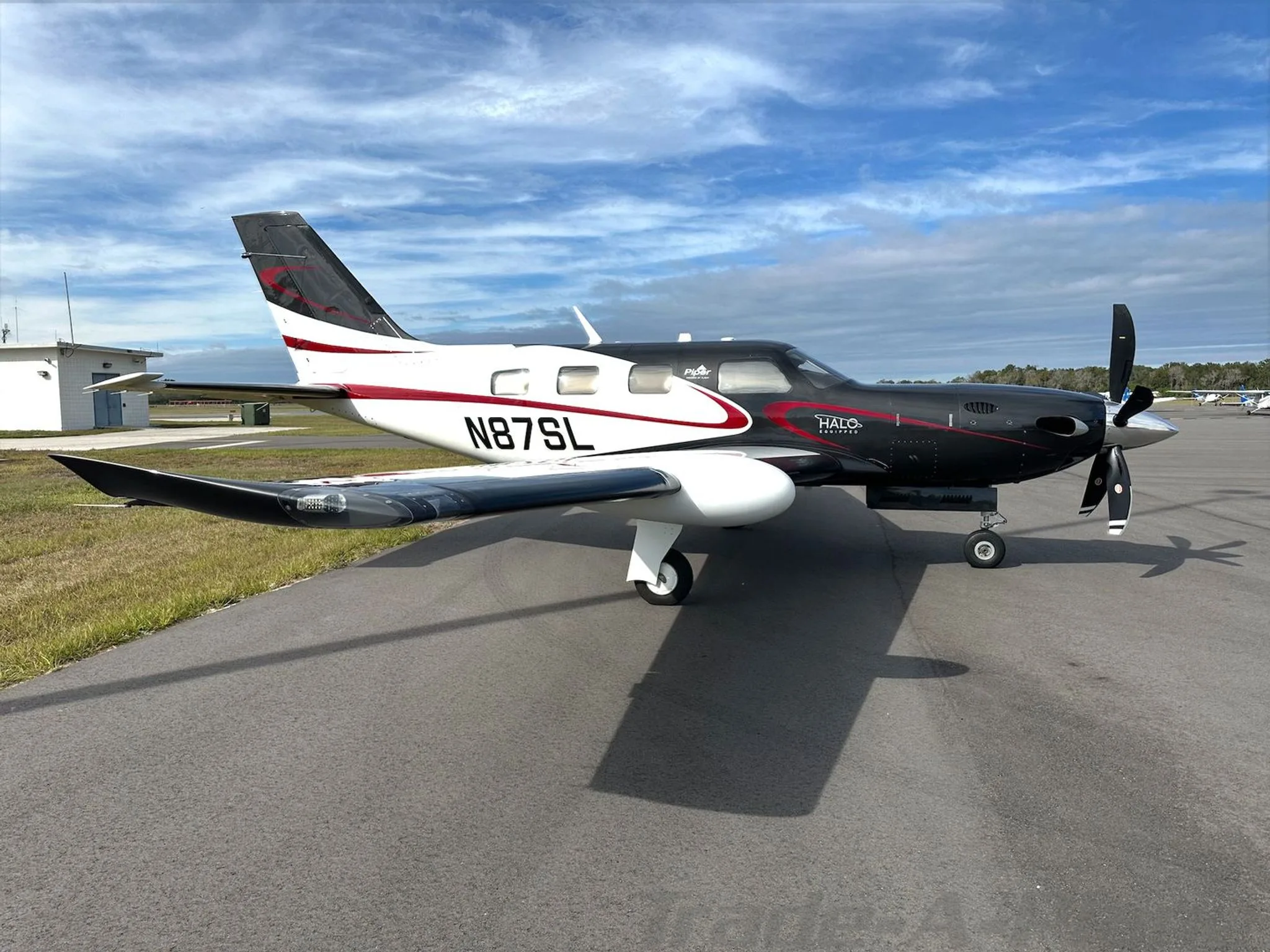 A Piper M600/SLS aircraft with a black and white paint scheme, red accents, and registration N87SL, parked on an airfield.