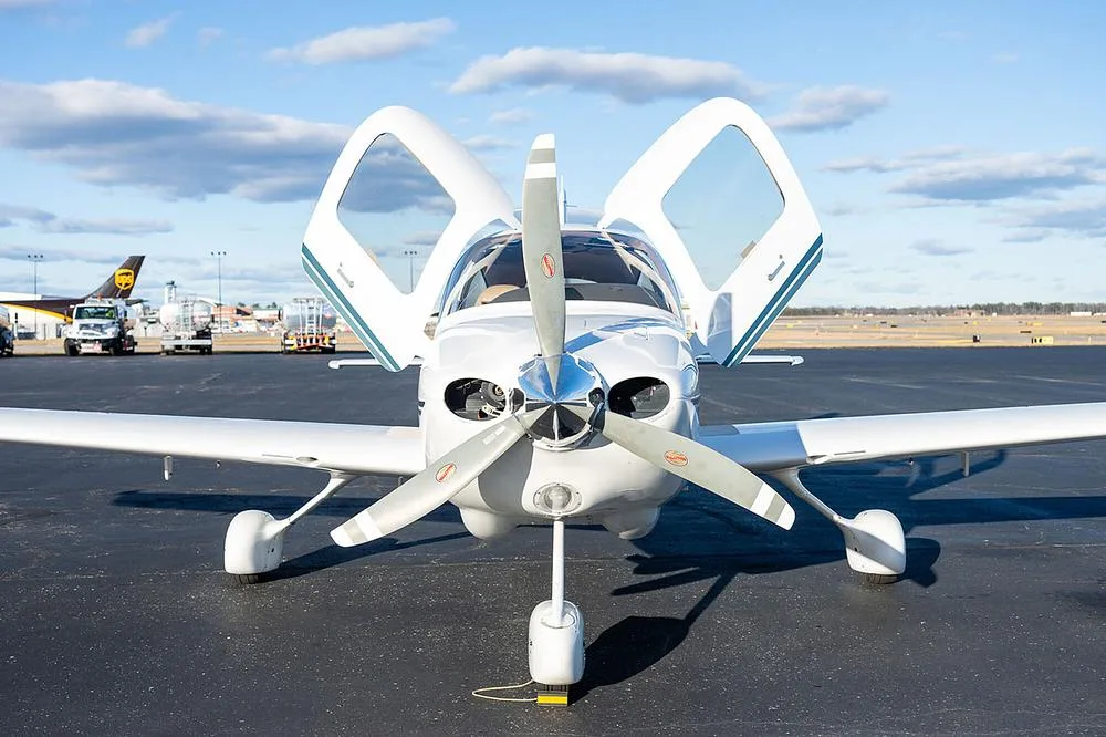 A head-on view of a white Cirrus SR20 aircraft, registration N639DR, with its gull-wing doors open, parked on an asphalt tarmac.