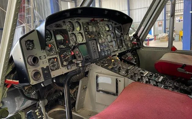 The detailed instrument panel and control console of a helicopter cockpit with a red seat visible.