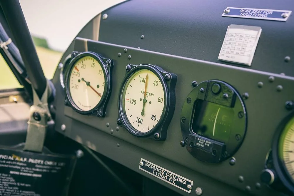 A close-up of a vintage aircraft's instrument panel, featuring an airspeed indicator, tachometer, and other gauges.