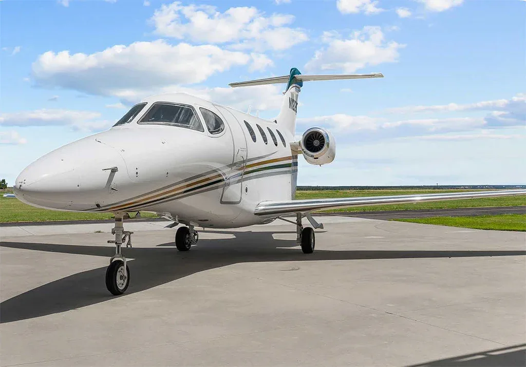 A white private jet with green and gold stripes on the tail and fuselage, parked on an airfield under a blue sky.