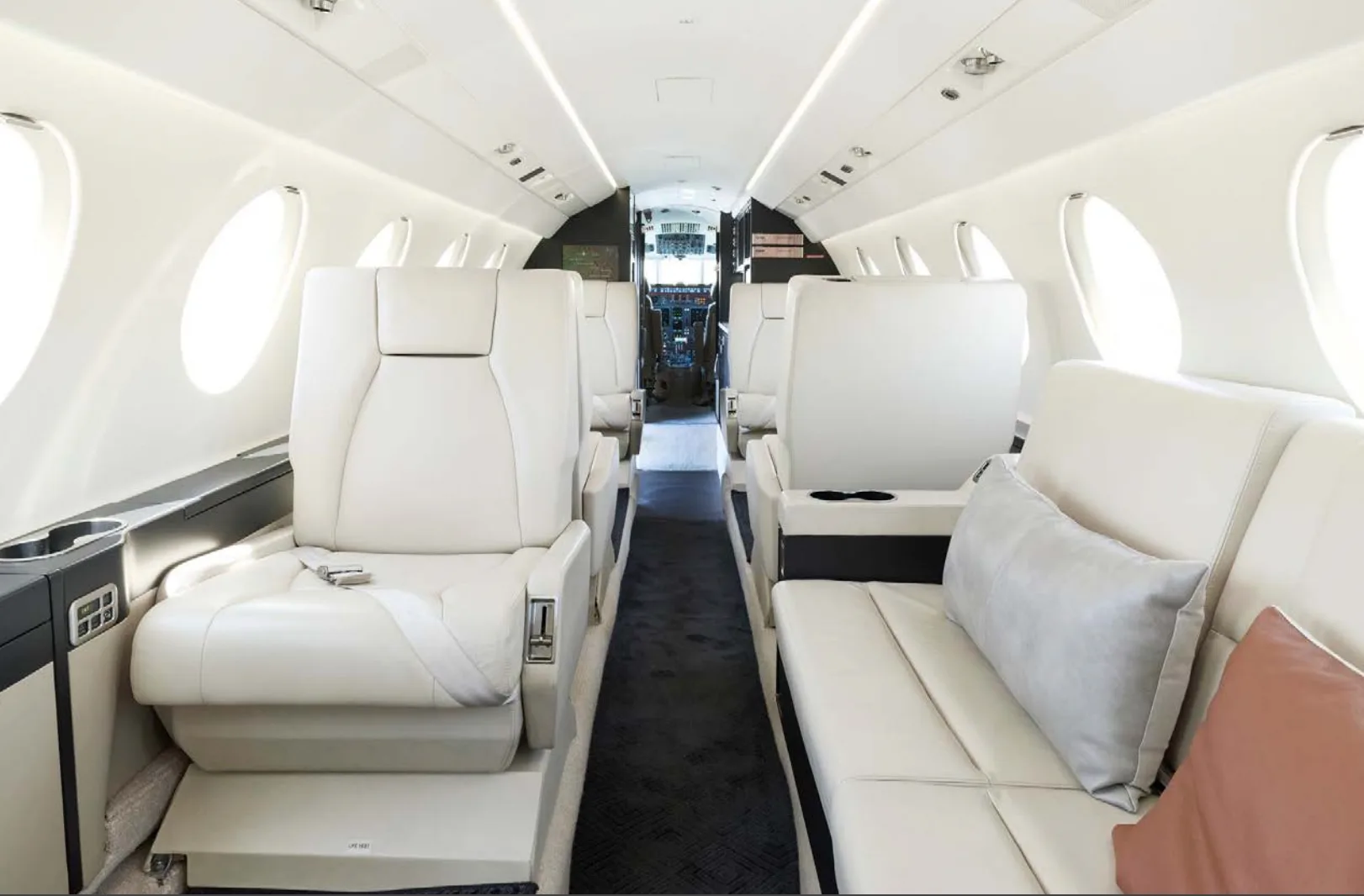 The spacious interior of a private jet cabin features cream-colored seating arrangements and a view towards the cockpit.