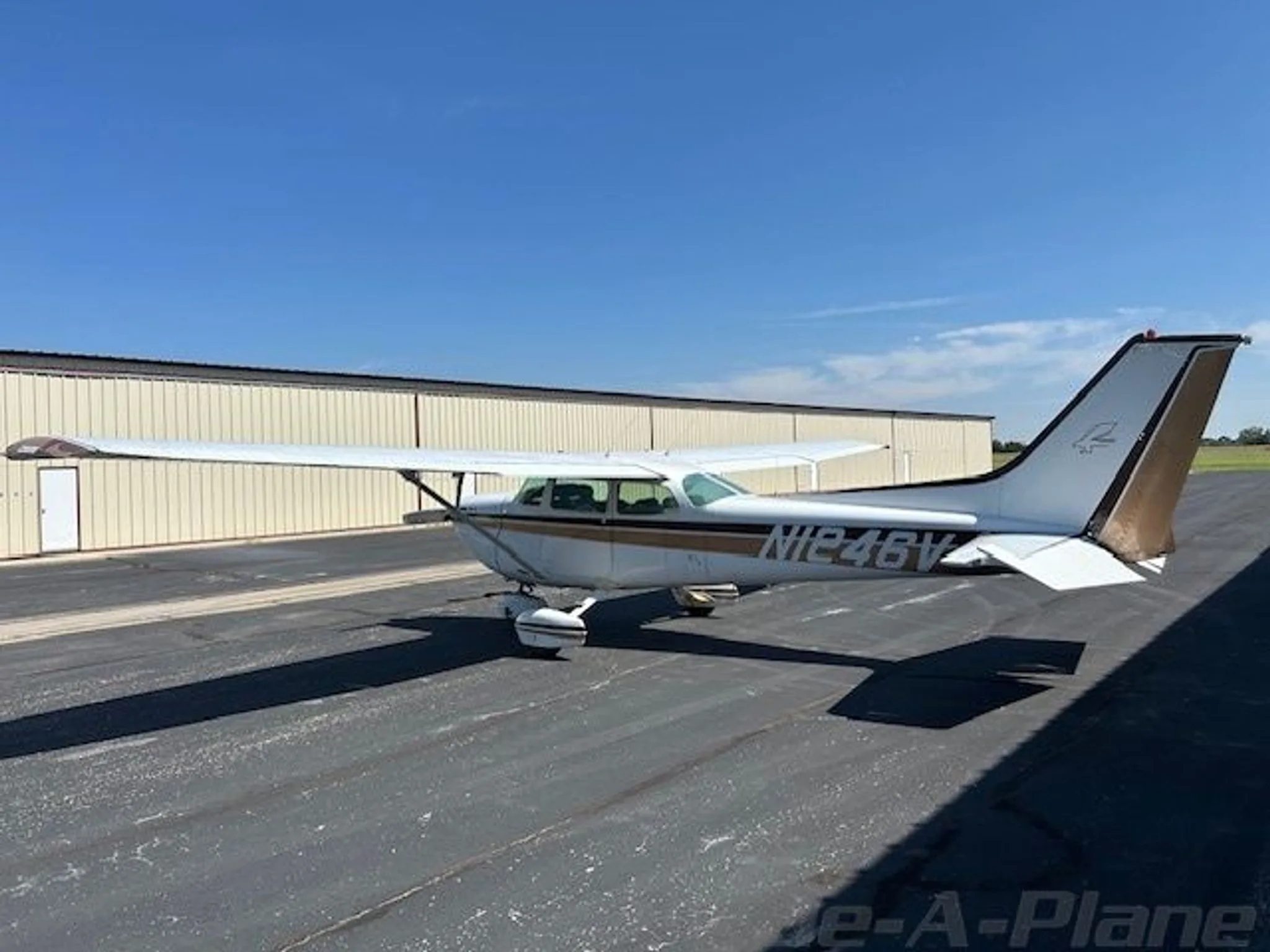 Three-quarter rear view of a white and brown Cessna R172K (N1246V) on an asphalt ramp.