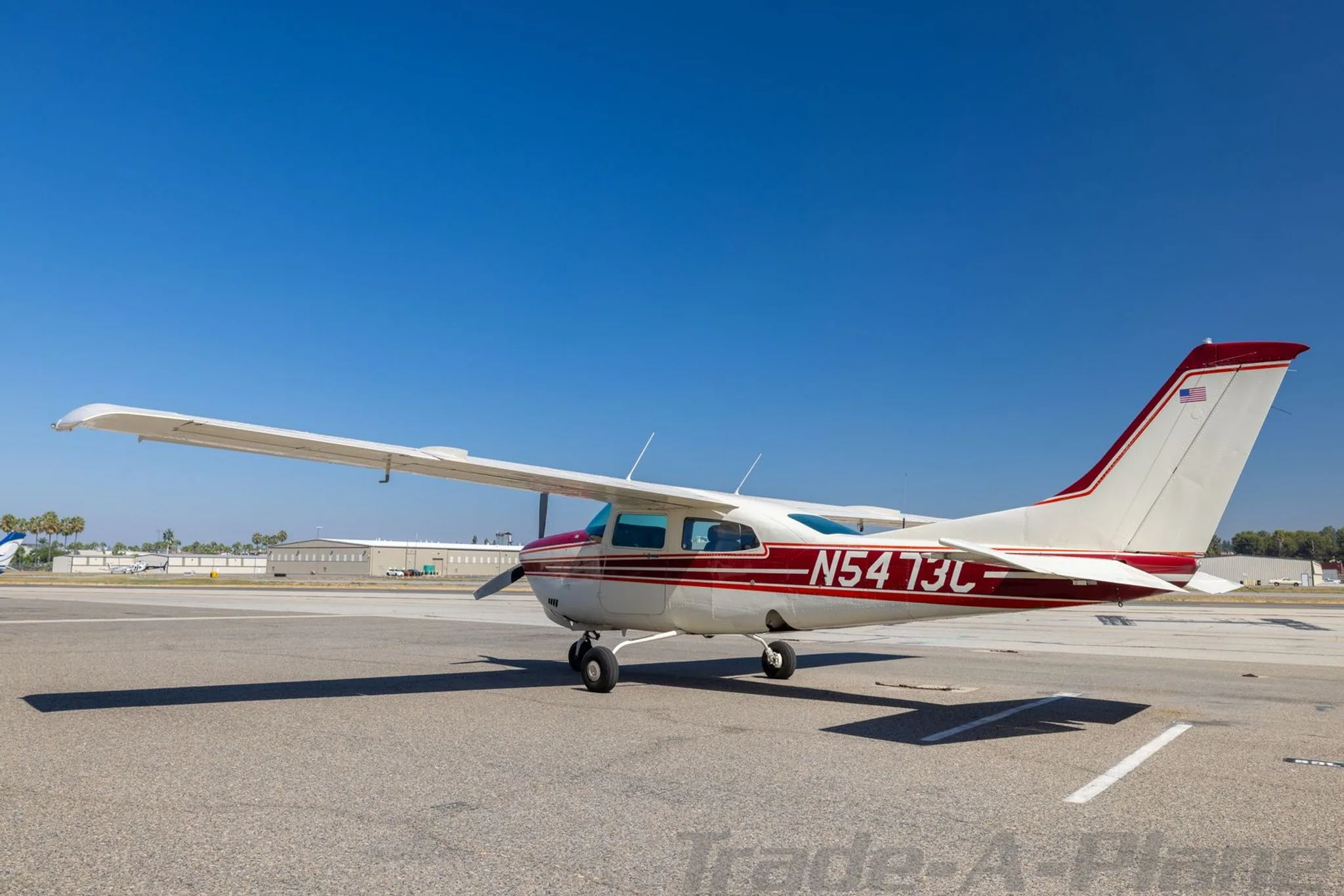 A side view of a white and red Cessna 210 Centurion aircraft, tail number N5473C, parked on an asphalt tarmac.