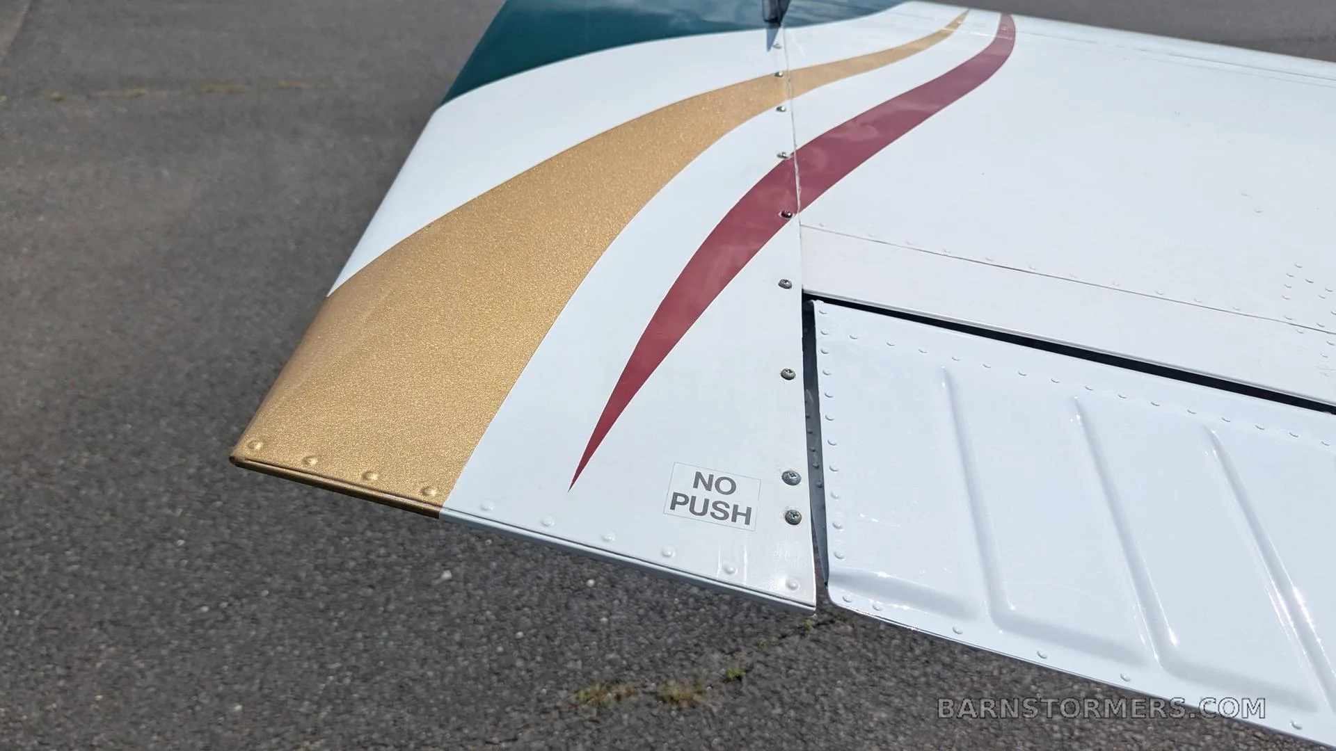 A close-up of the wingtip of the Beechcraft Bonanza, featuring gold and maroon stripes and a "NO PUSH" label.