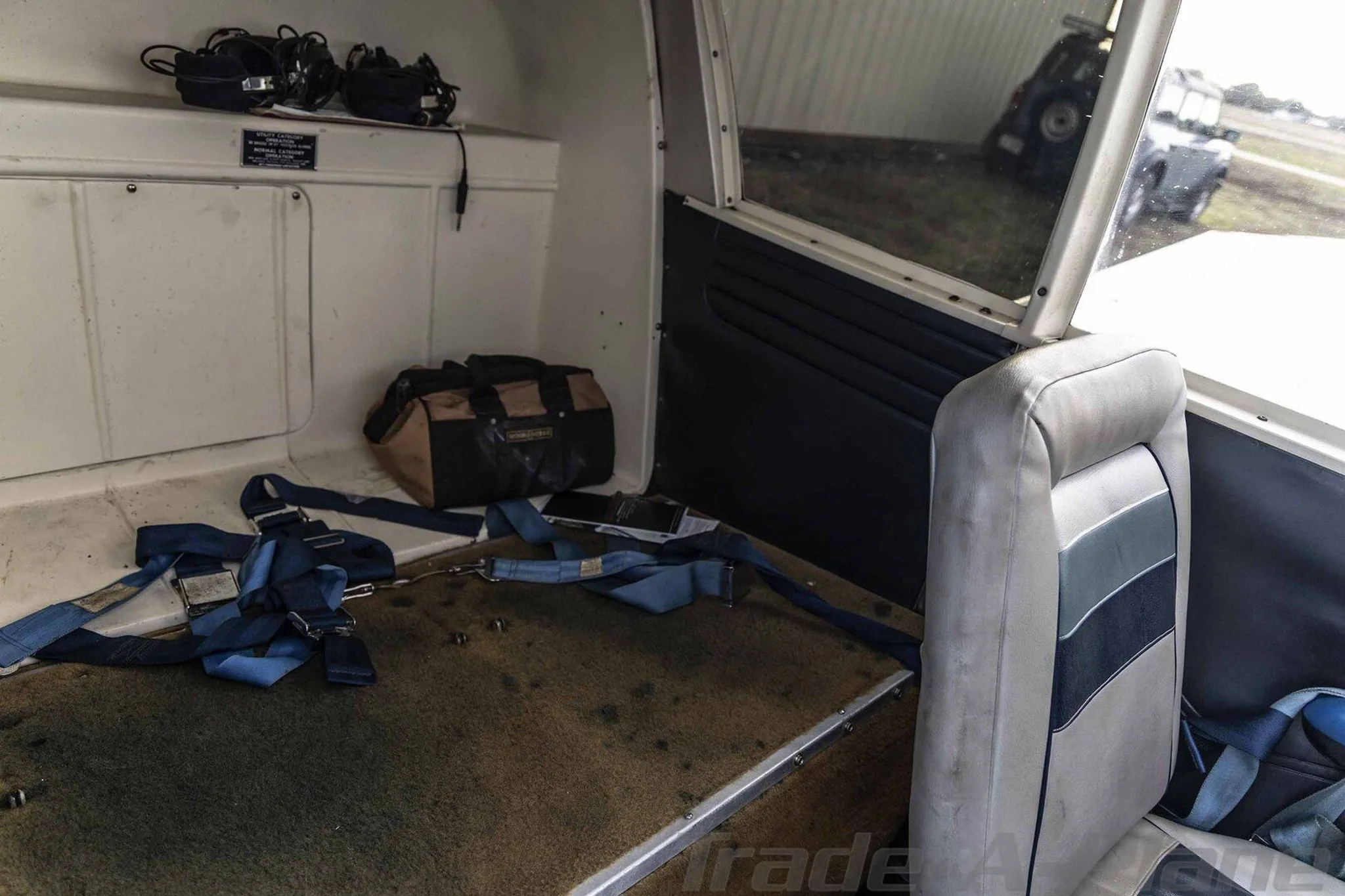The rear cabin area of the Piper Cherokee, showing a single seat, a bag, and blue straps on the floor.