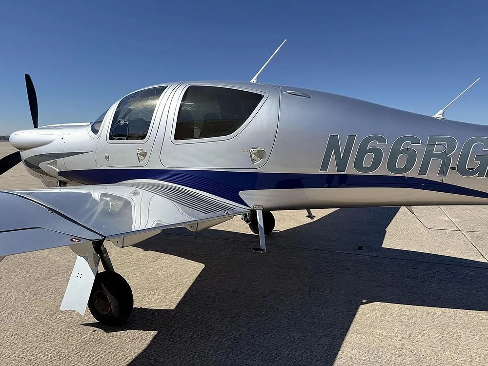 A close-up view of the fuselage and wing of the silver and blue Diamond DA40 aircraft, N66RG, showing its registration.
