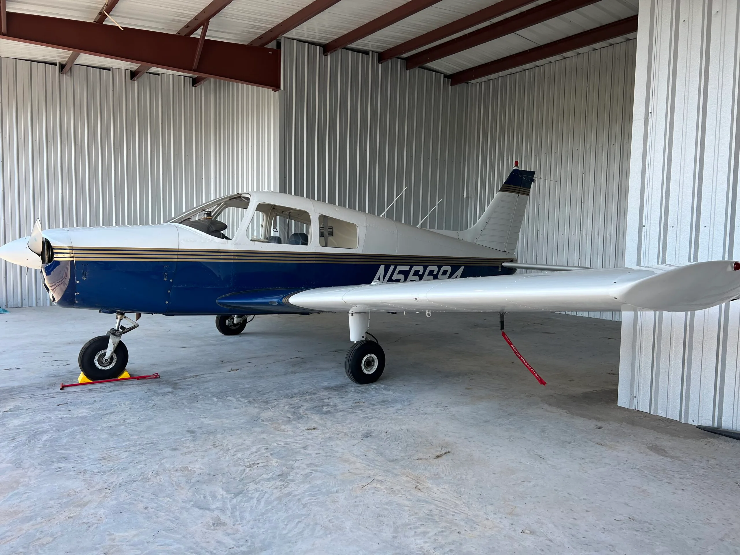 A white and blue light aircraft with gold stripes, registration N15684, parked inside a hangar.