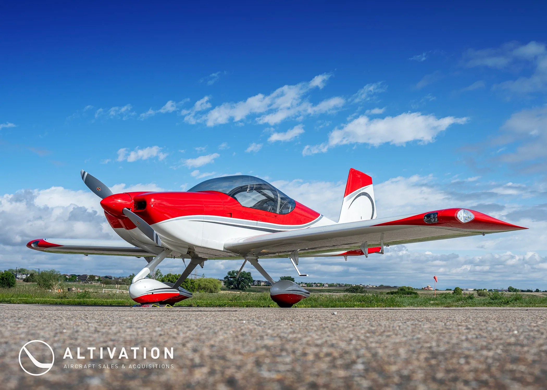 A low-angle front-side view of the red and white N918ZH aircraft under a bright blue sky with scattered clouds.