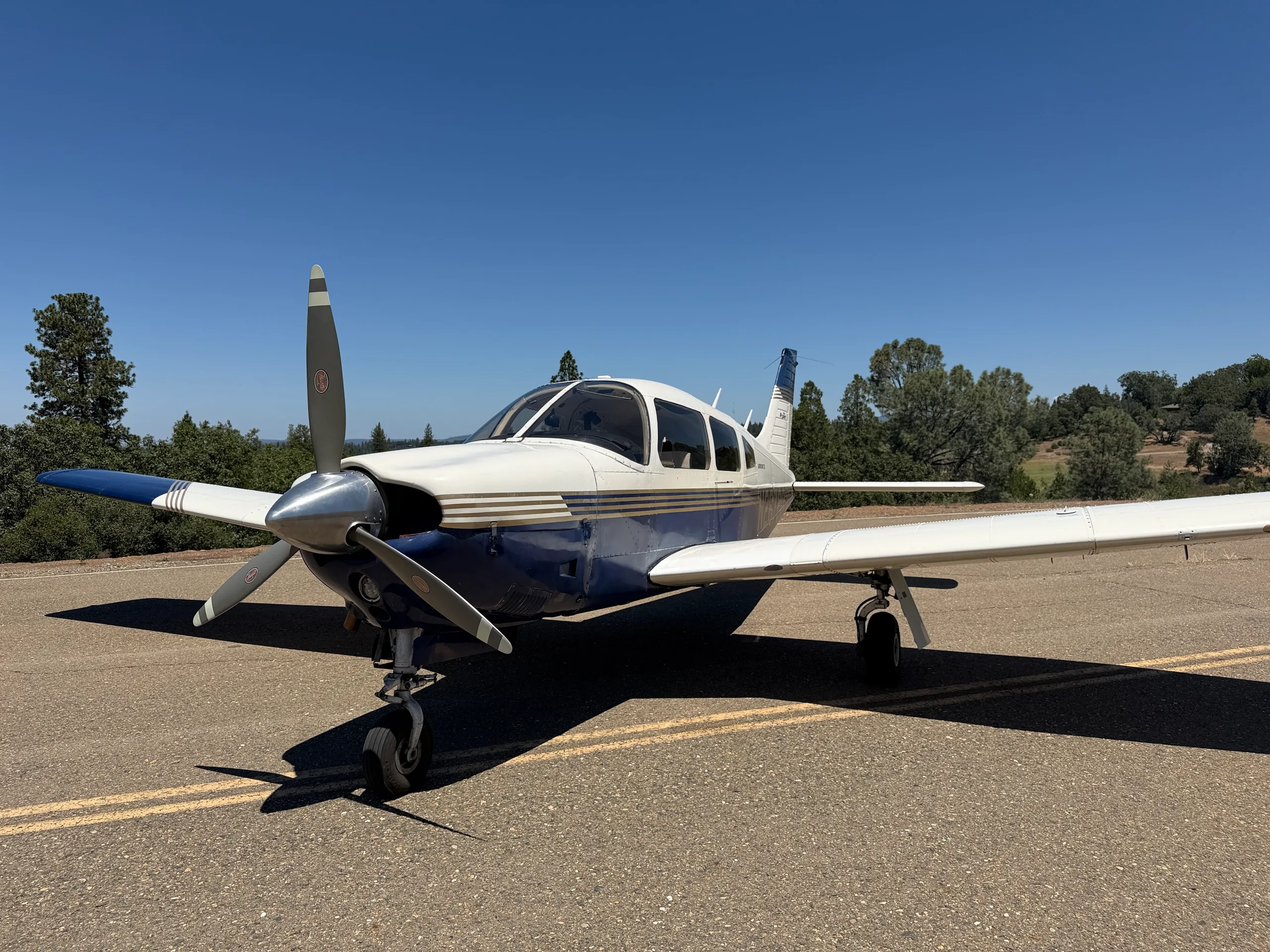A front-quarter view of a white and blue Piper Arrow III aircraft, tail number N2672Q, parked on an asphalt surface.