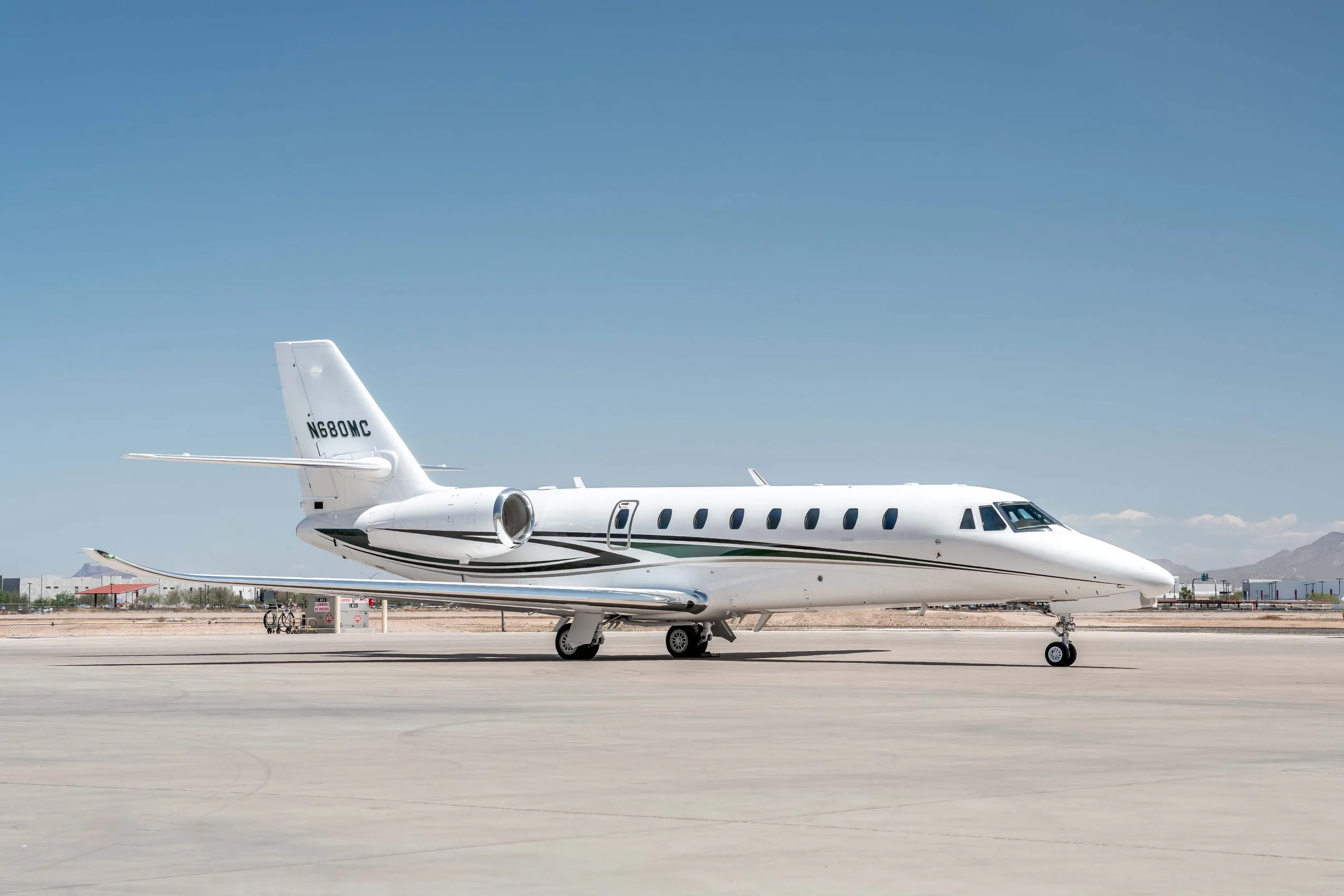 A white Cessna Citation Latitude business jet with black and green stripes, registration N680MC, parked on a sunny tarmac.