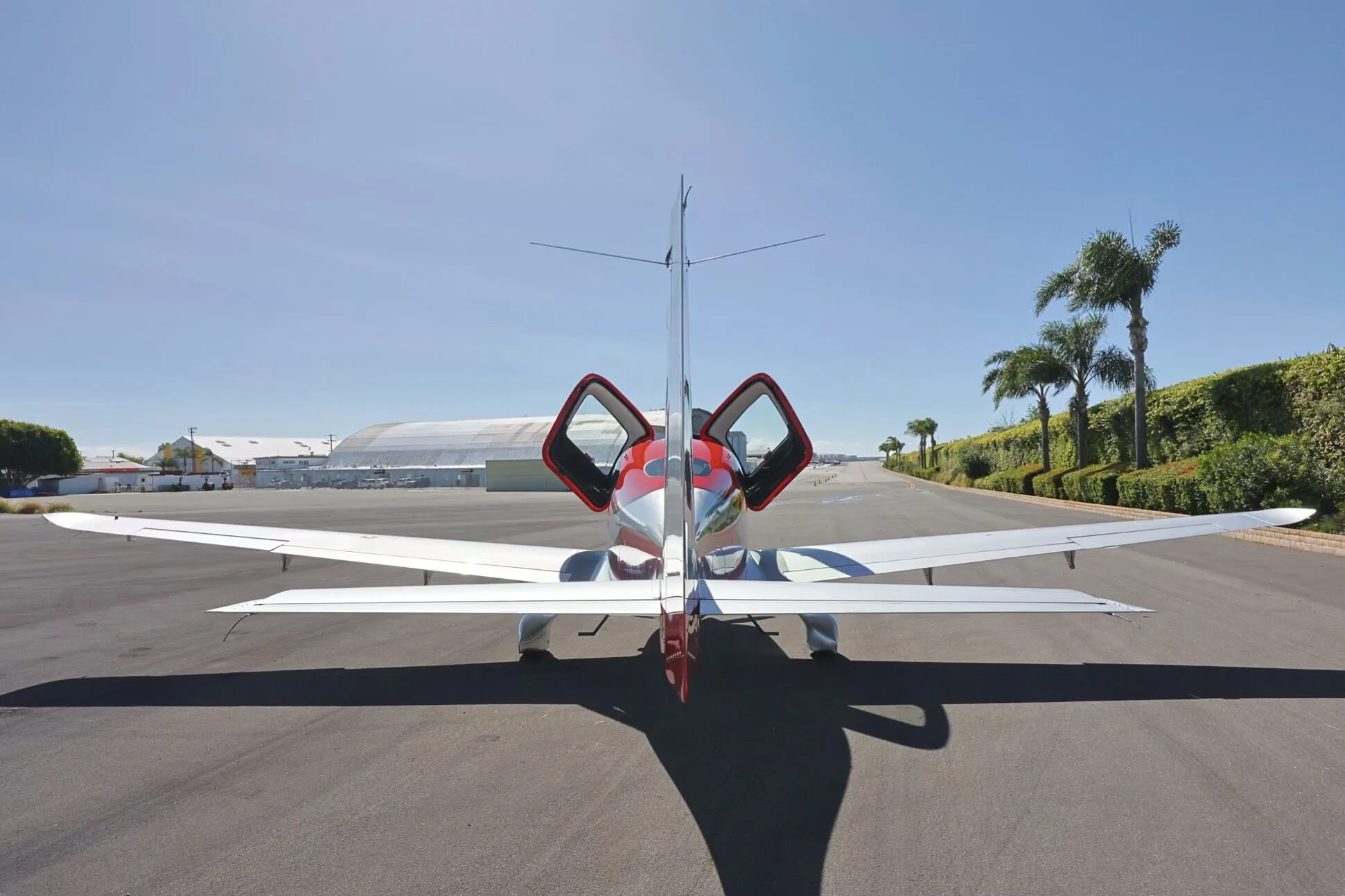 A rear view of the red and silver Cirrus SR22 GTS aircraft, N245WP, with its gull-wing doors open.