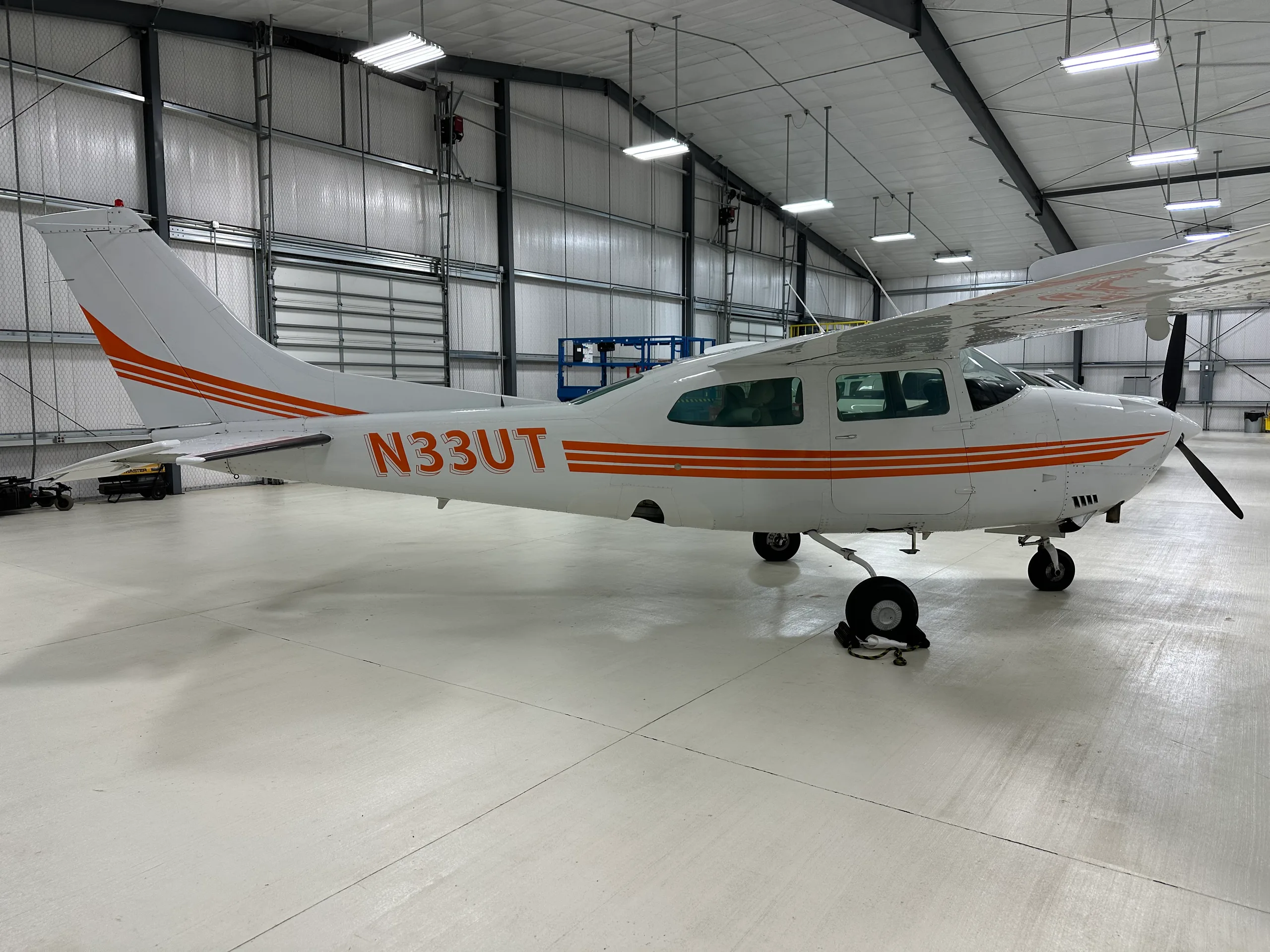 A Cessna 206 Stationair aircraft with orange stripes parked in a hangar.