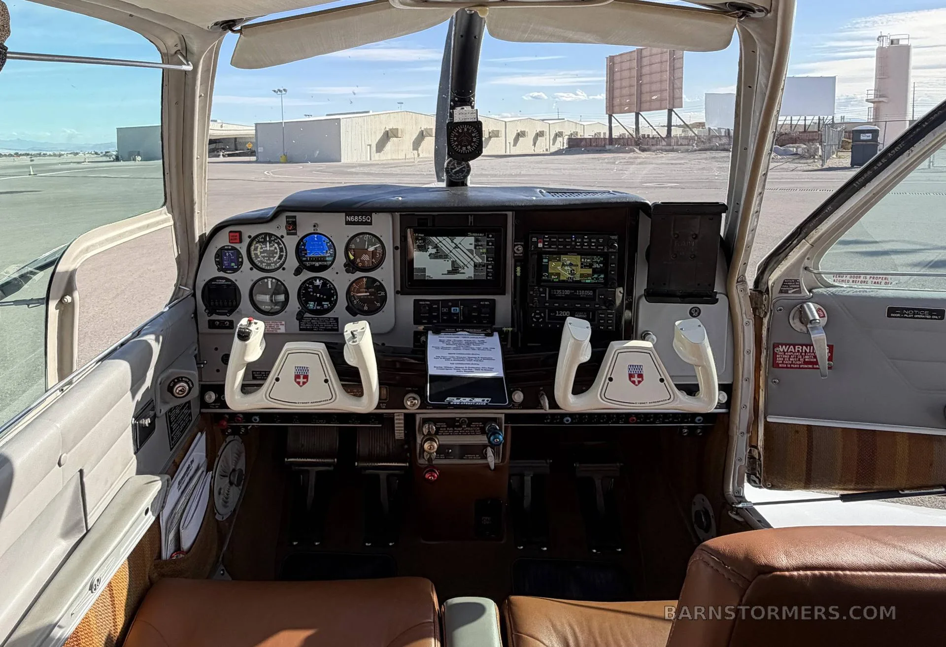 The cockpit of the Beechcraft Bonanza N68550, showing the instrument panel, yokes, and brown leather seats.