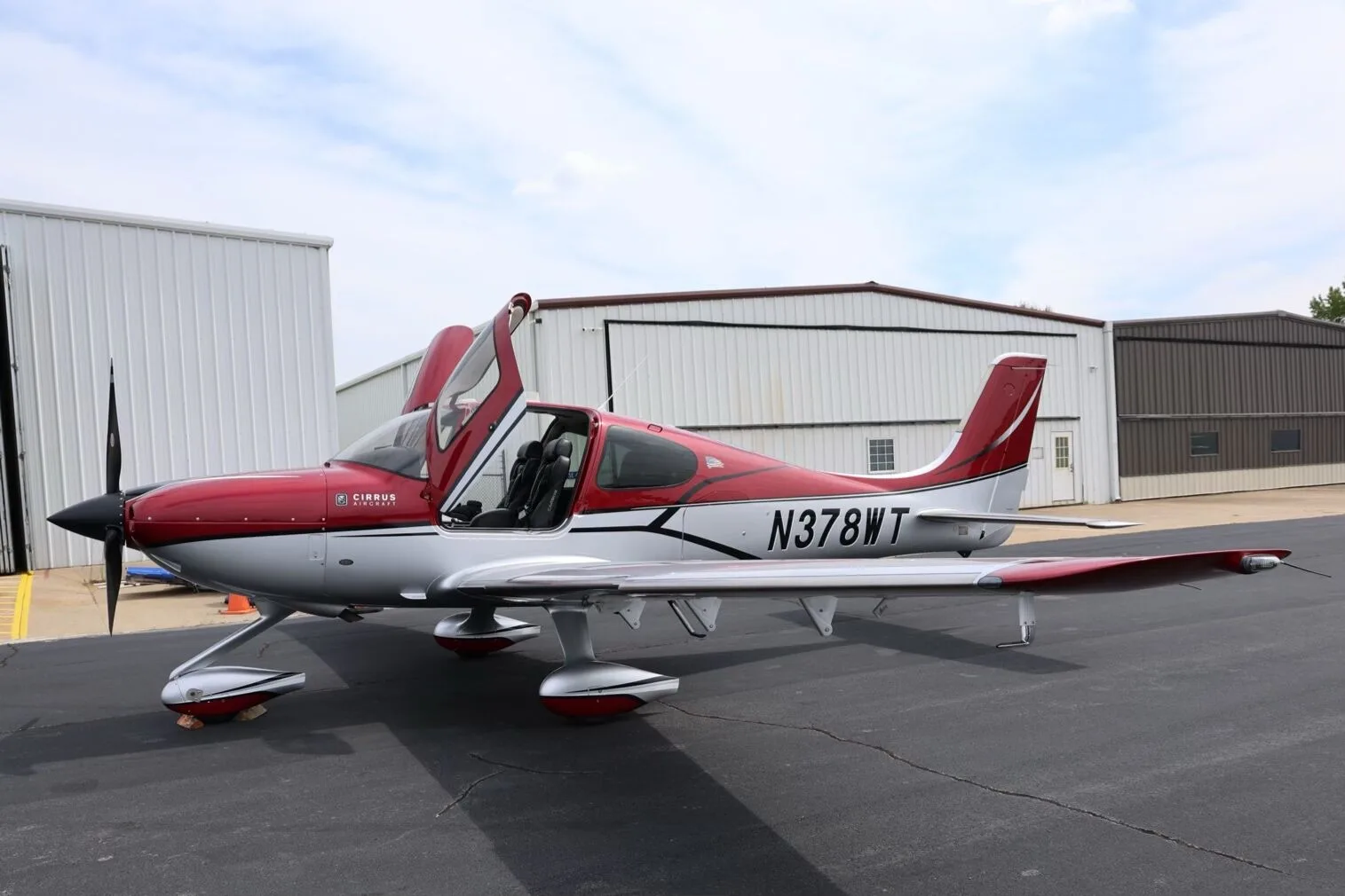 A red and silver Cirrus SR22T aircraft, N378WT, with its doors open, parked on an airfield tarmac.