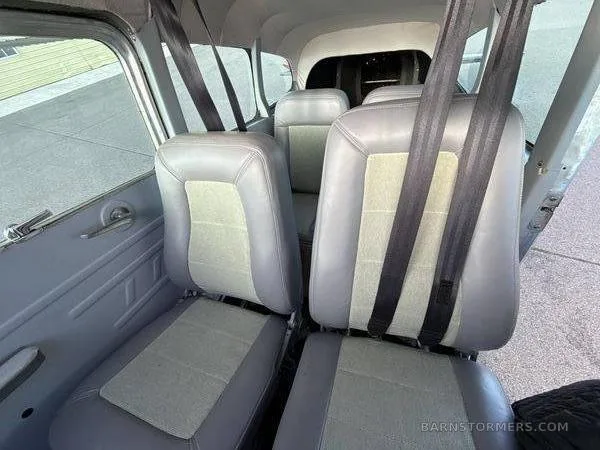 The interior cabin of a small aircraft, showing two rows of grey and light-colored seats with seatbelts.
