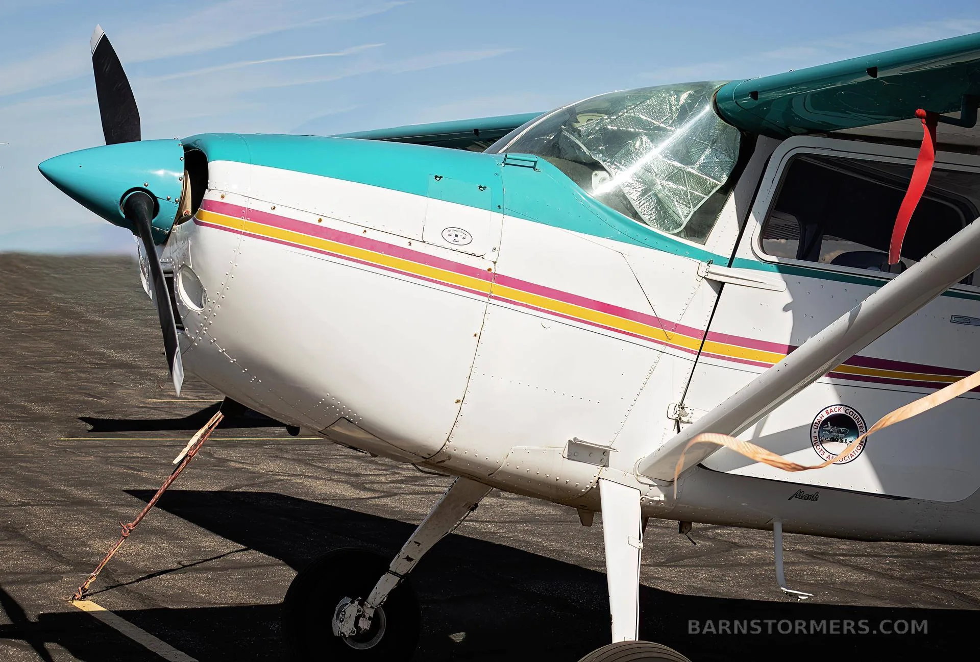 Close-up front-left view of a white and teal single-engine propeller aircraft with pink and yellow stripes.