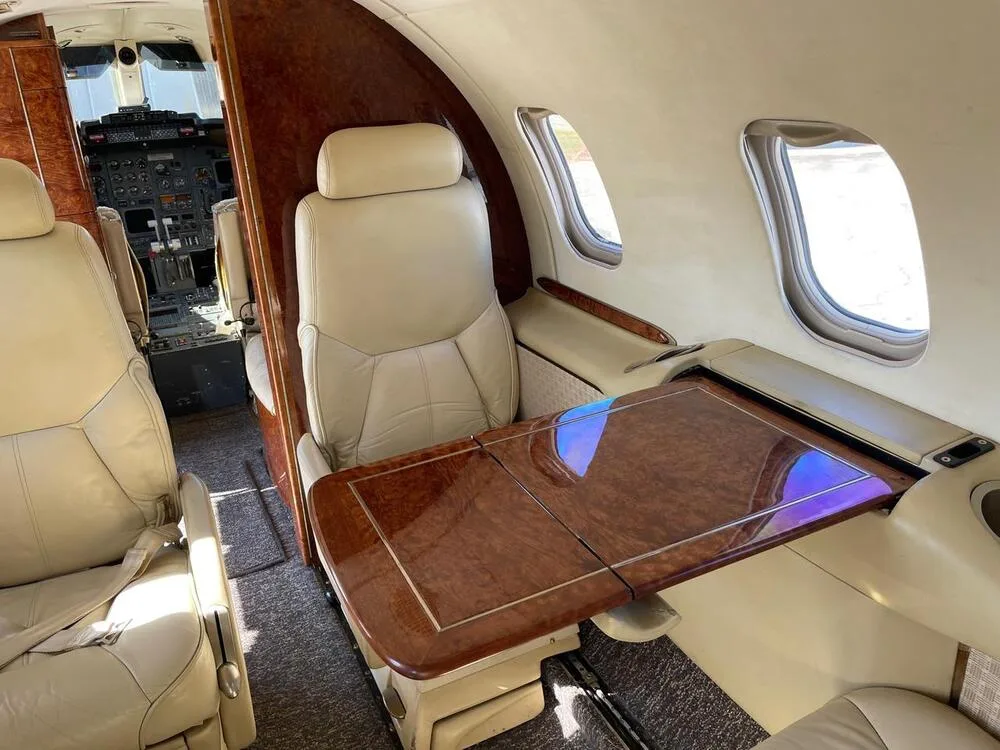 A section of the aircraft cabin featuring a beige leather seat and a polished wooden fold-out table.