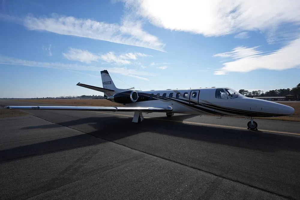 A side profile of the Cessna Citation Encore business jet N560CB, with its distinctive black and gold livery, on an airfield.