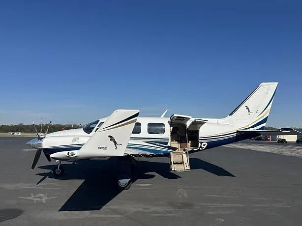 A white and blue twin-engine propeller aircraft with "Panther" logo and registration N59809 on the tail, parked on an asphalt tarmac with its passenger door open.