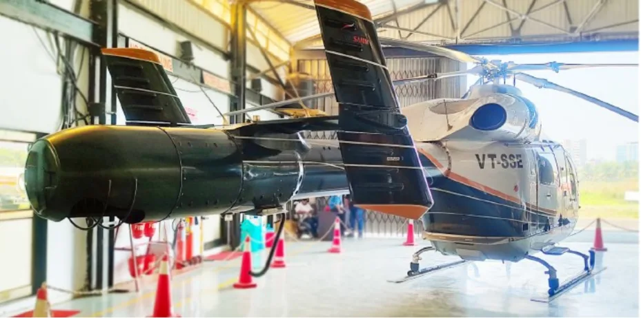 The rear view of a silver and black MD helicopter with registration VT-SSE, showing its NOTAR tail in a hangar.