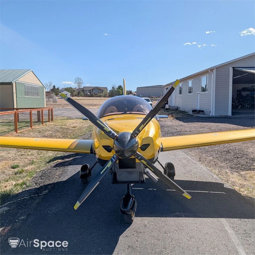A head-on view of a yellow and black Freccia F200 aircraft with a three-bladed propeller, parked on an asphalt ramp.