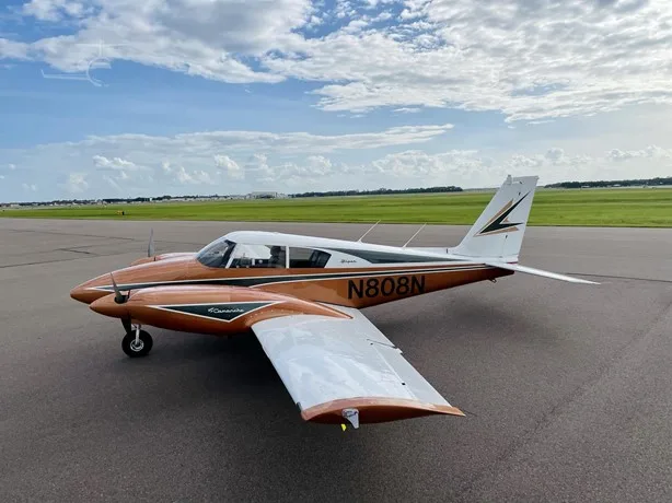 Side view of a copper and white Piper Comanche twin-engine aircraft with registration N808N on an airfield.