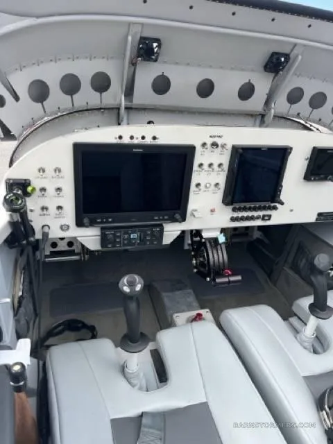 A view of the cockpit of a small aircraft, showing the instrument panel with two large screens, controls, and light gray seats.