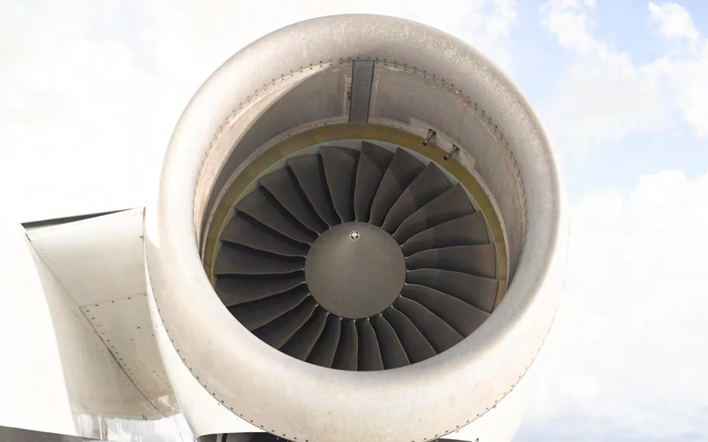 A close-up view of a jet engine intake with visible fan blades against a cloudy sky.