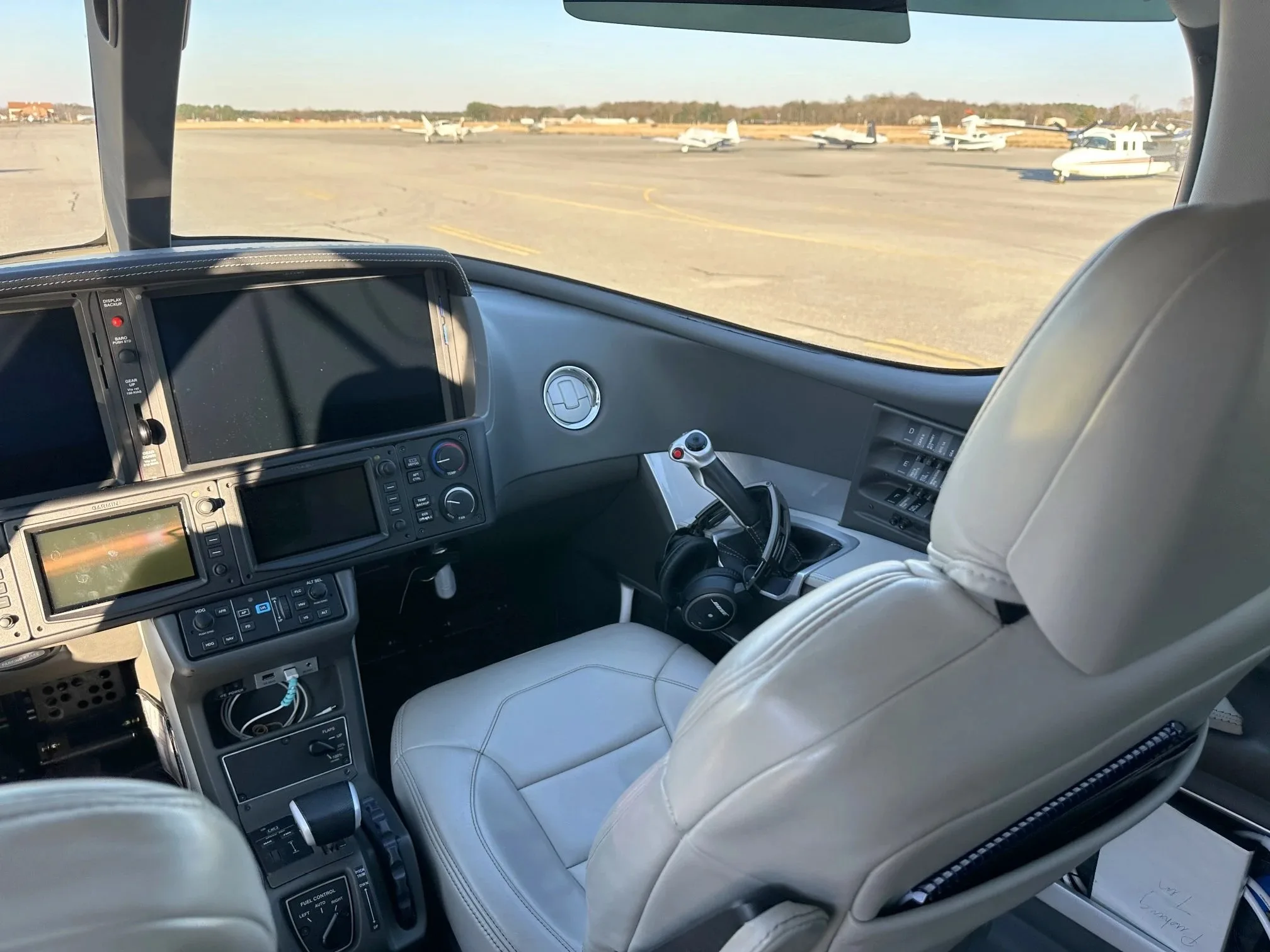 The cockpit of a Cirrus Vision Jet, viewed from the pilot's seat, looking out onto an airfield with other aircraft.