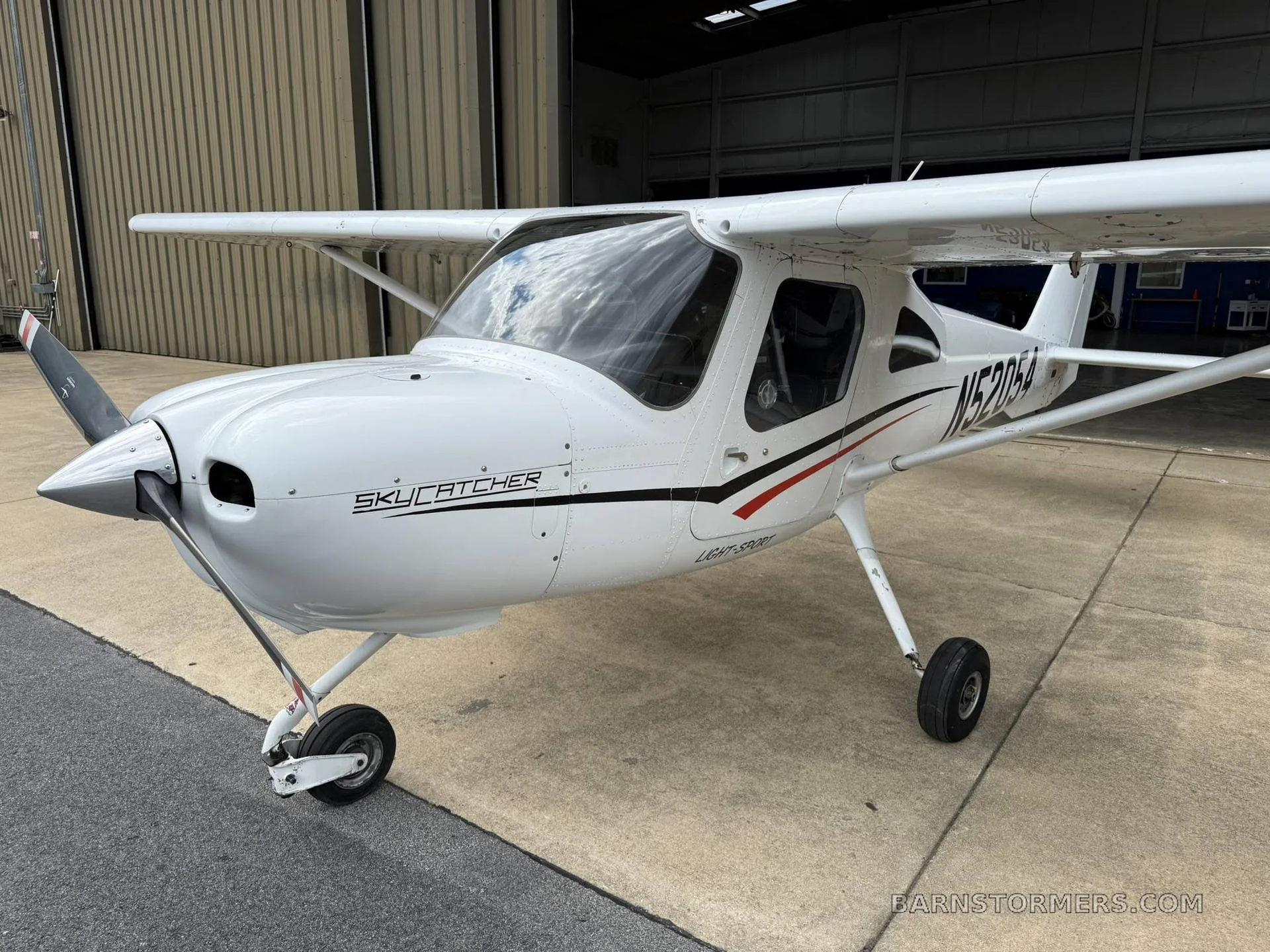 A white Cessna Skycatcher light-sport aircraft with black and red stripes, viewed from the front-left, parked outside a hangar.