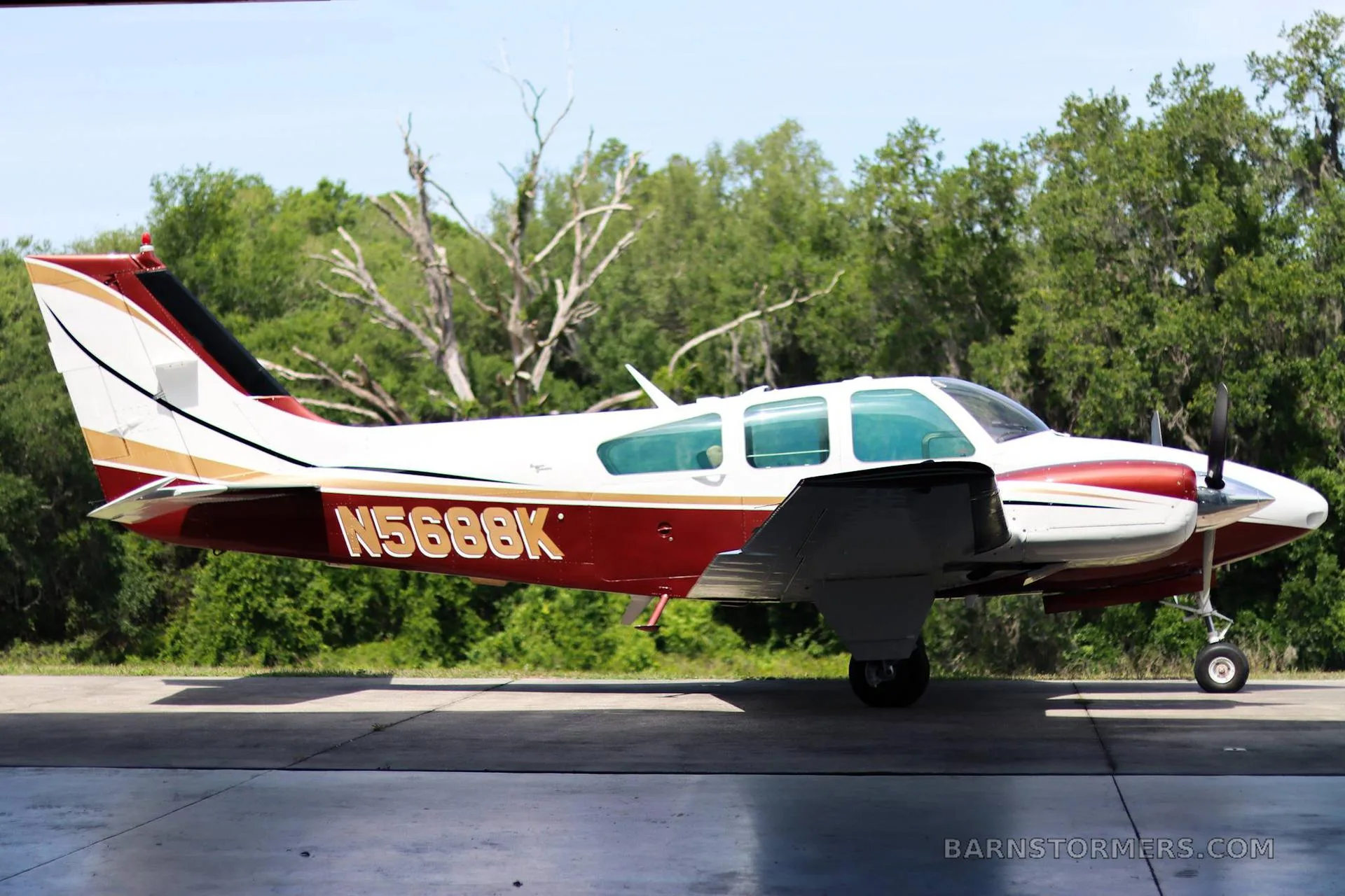 A side view of a white and maroon twin-engine propeller aircraft with registration N5688K, parked on a tarmac.