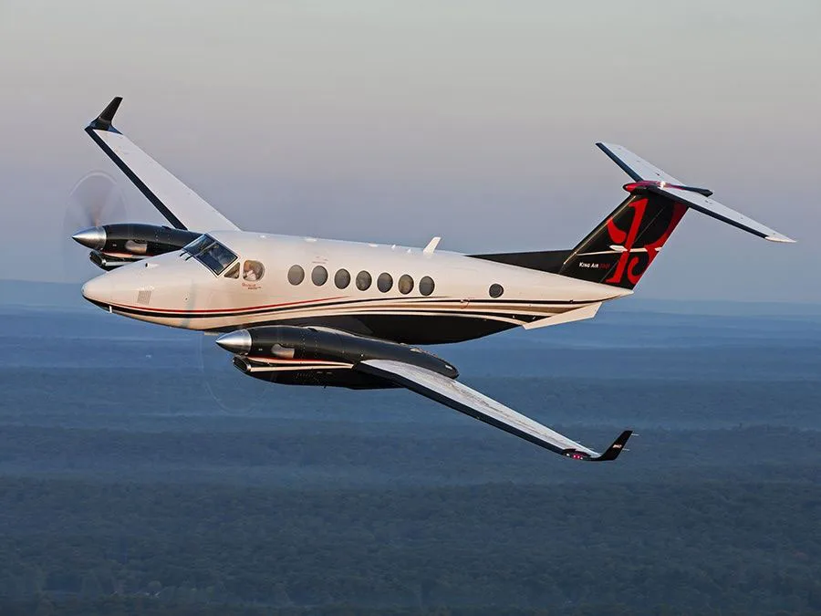 King Air 350i in flight over a wooded area.
