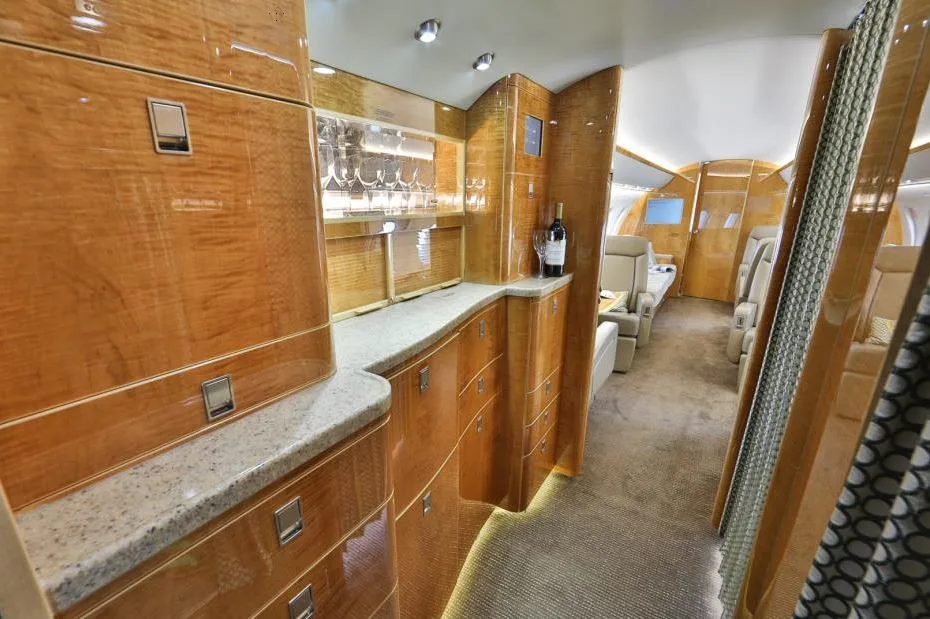 The aircraft's galley area features polished wood cabinetry, a granite-like counter, and a display of glassware.
